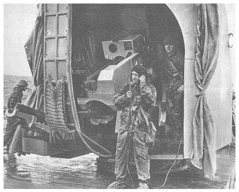 Zeitschriftenreproduktion: Behelmte Geschützbedienung in Schutzkleidung am offenen 100-mm-Geschützturm, ein Matrose spricht in ein Kehlkopfmikrofon